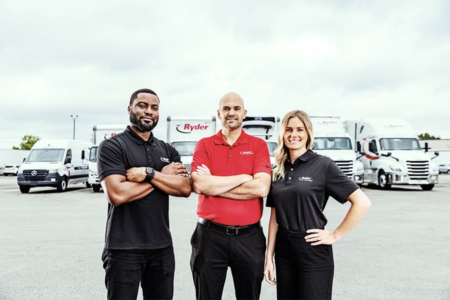 Three Ryder truck drivers posing in front of a fleet of trucks